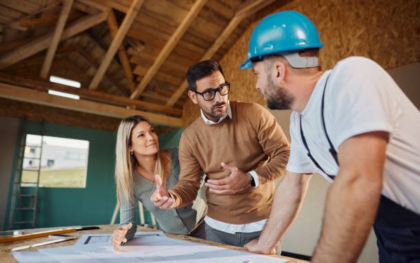 Young couple talking to manual worker about housing design plans at construction site.
